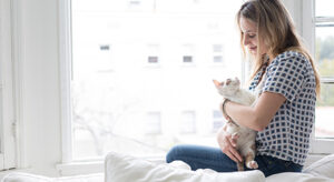 Frau sitzt vor Fenster mit Katze im Arm