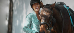 Lachende Reiterin mit Helm steht bei Pferd