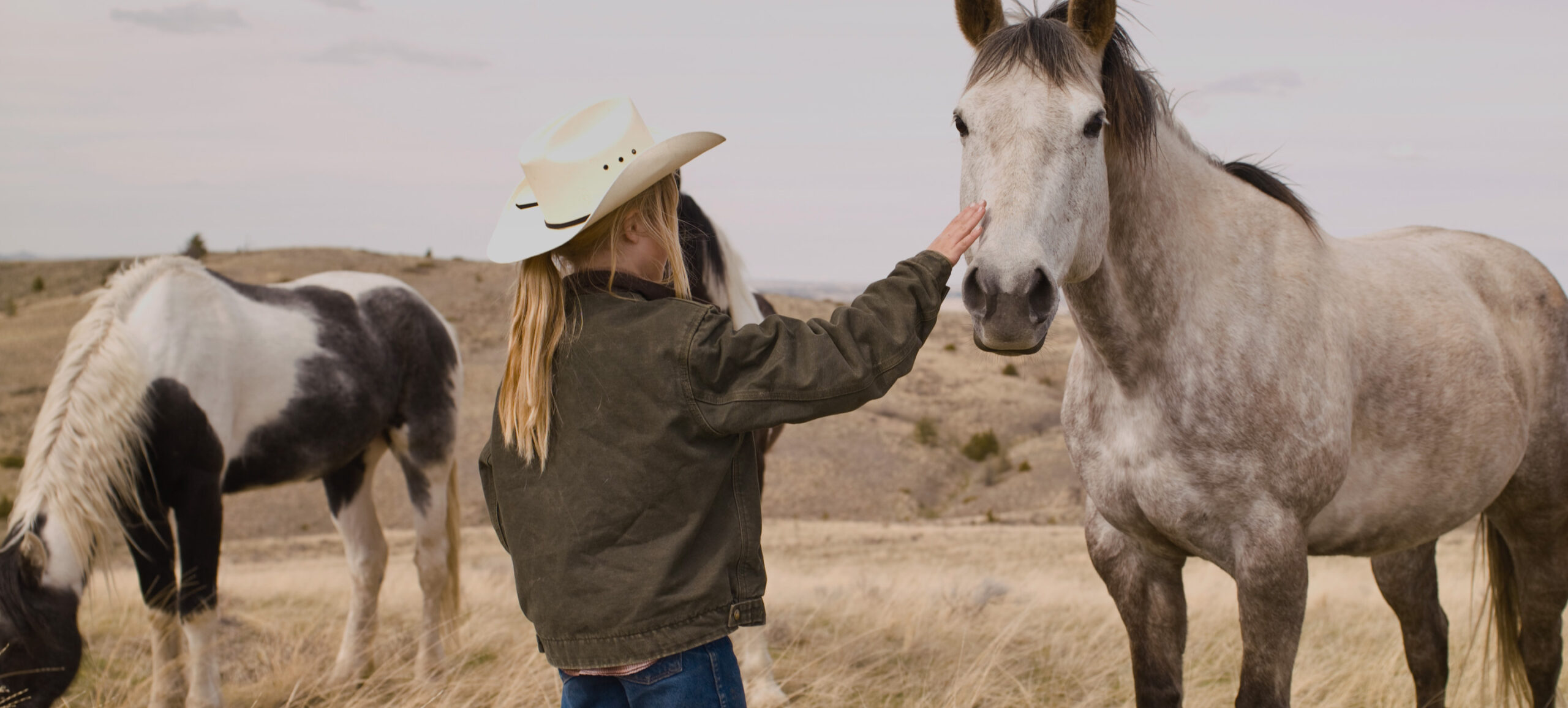 Mädchen mit Westernhut streichelt Pferd in Steppe