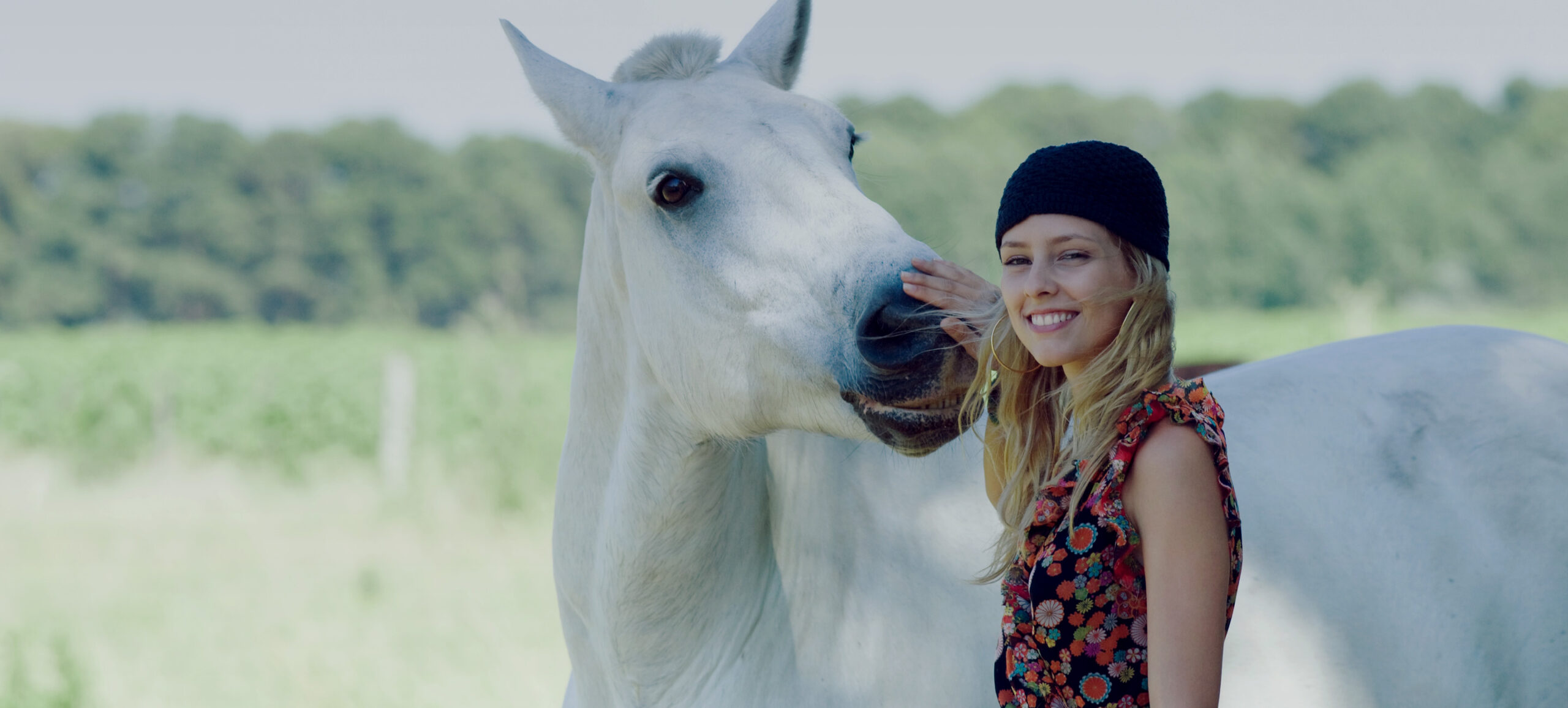 Mädchen mit Mütze legt Hand auf Nase eines Pferdes