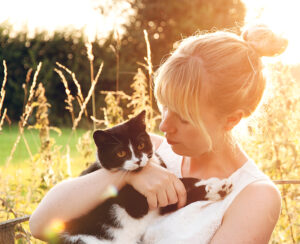 Schwarz-weiße Katze auf Arm von Besitzerin draußen im sommerlichen Garten. Die Katze genießt eine Katzen-Krankenversicherung der Uelzener.