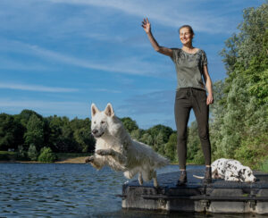 Frau winkt in die Ferne während Hund ins Wasser springt