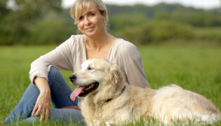 Junge Frau sitzt mit ihrem Patenhund aus dem Tierheim auf einer grünen Wiese, der Hund schaut zufrieden in die Ferne.
