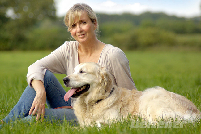 Junge Frau sitzt mit ihrem Patenhund aus dem Tierheim auf einer grünen Wiese und der Hund schaut zufrieden in die Ferne.