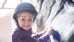 Ein kleines Kind putzt sein Trainingspferd, wenn Kinder reiten lernen ist Sicherheit am wichtigsten.