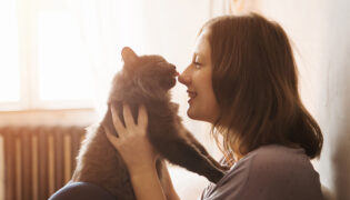 Frau kuschelt mit Katze, Haustiere wirken sich oft auf die Gesundheit aus.