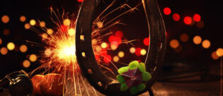 Hufeisen mit Sektkorken und einem vierblättrigen Kleeblatt sowie einer brennenden Wunderkerze im Hintergrund.