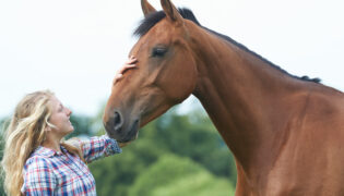 Blonde Frau streichelt ihrem braunem Pferd über die Nase