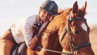 Mädchen sitzt lachend auf einem Pferd. Erfüllt sie das Bild eines Pferdemädchens?