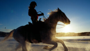 Eine Frau reitet mit ihrem Pferd in einer Schneeprärie durch den Sonnenaufgang