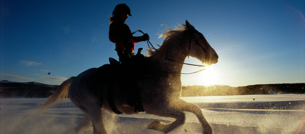 Eine Frau reitet mit ihrem Pferd in einer Schneeprärie durch den Sonnenaufgang