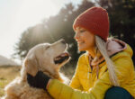 Junge Frau mit gelber Jacke streichelt Golden Retriever Hund auf einem Hügel