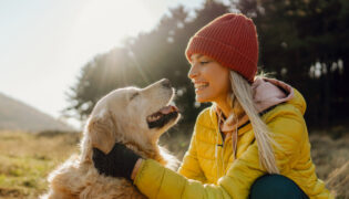 Junge Frau mit gelber Jacke streichelt Golden Retriever Hund auf einem Hügel