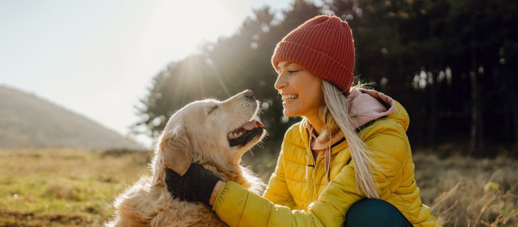 Junge Frau mit gelber Jacke streichelt Golden Retriever Hund auf einem Hügel