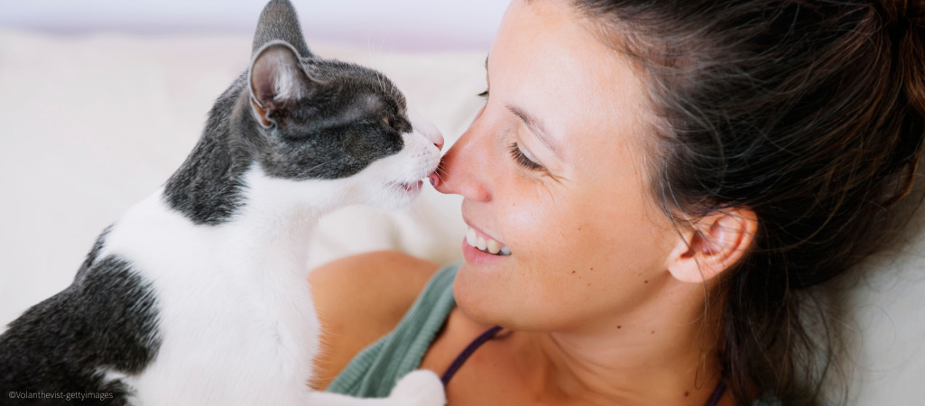 Auf dem Foto ist eine schwarz weiße Katze zu sehen, sie leckt ihre Halterin an der Nase ab.