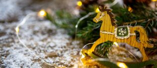 Ein braunes kleines Schaukelpferd steht auf einem mit Schnee bedecktem Stallboden vor einem Tannenzweig.