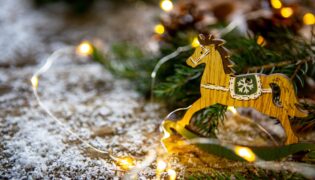 Ein braunes kleines Schaukelpferd steht auf einem mit Schnee bedecktem Stallboden vor einem Tannenzweig.