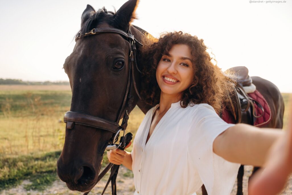 Eine junge Frau macht ein Selfie mit ihrem Pferd in natürlicher Umgebung.