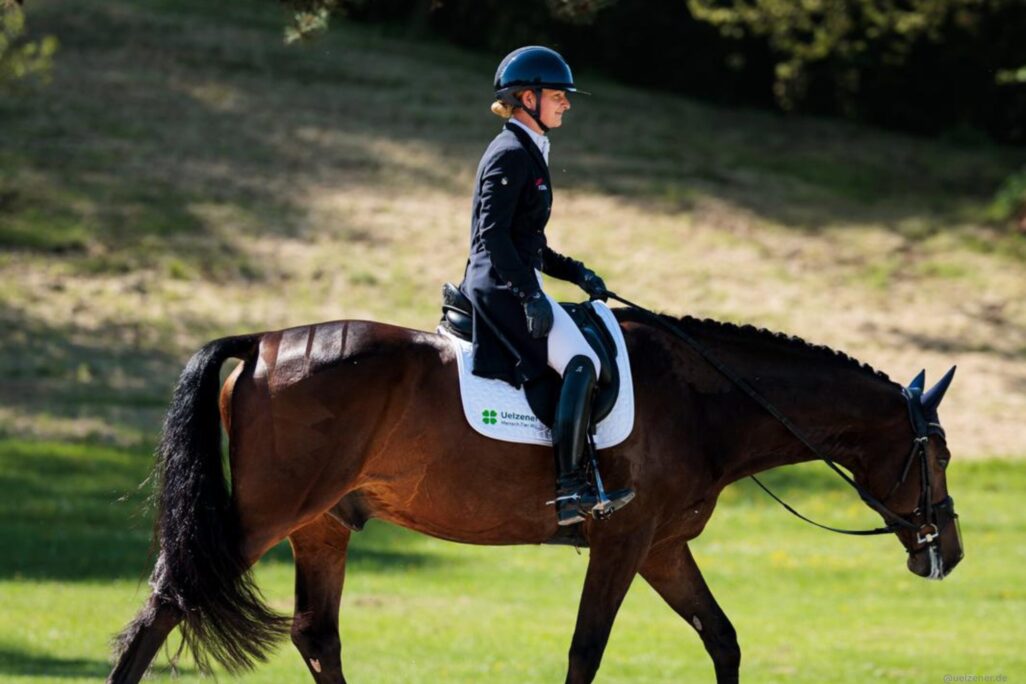 Julia Krajewski reitet auf ihrem Pferd auf einer grünen Weide.
