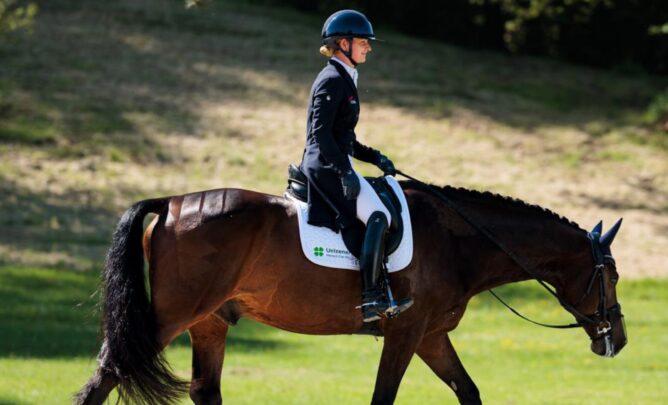 Julia Krajewski reitet auf ihrem Pferd auf einer grünen Weide.