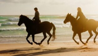 Zwei reitende Frauen am Strand.