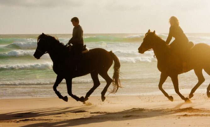Zwei reitende Frauen am Strand.