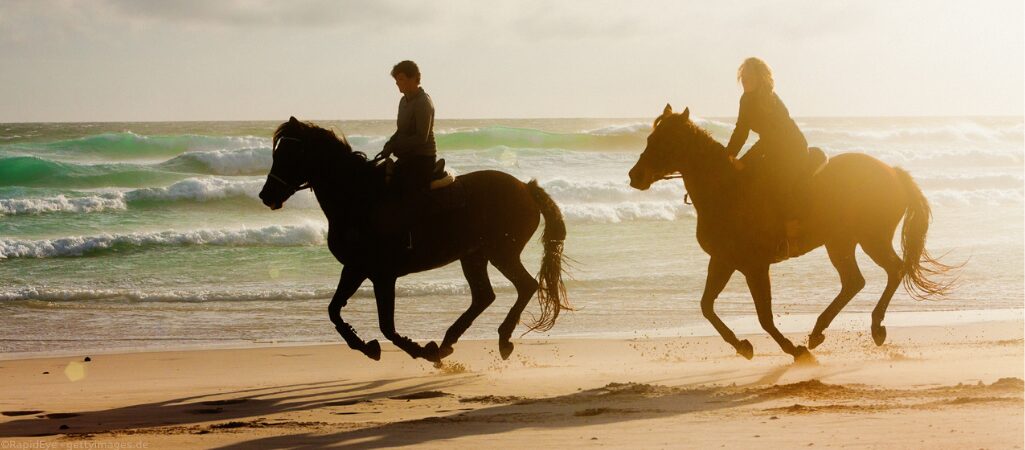 Zwei reitende Frauen am Strand.