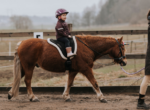 Reitlehrerin führt Kind auf Pferd über den Trainingsplatz.