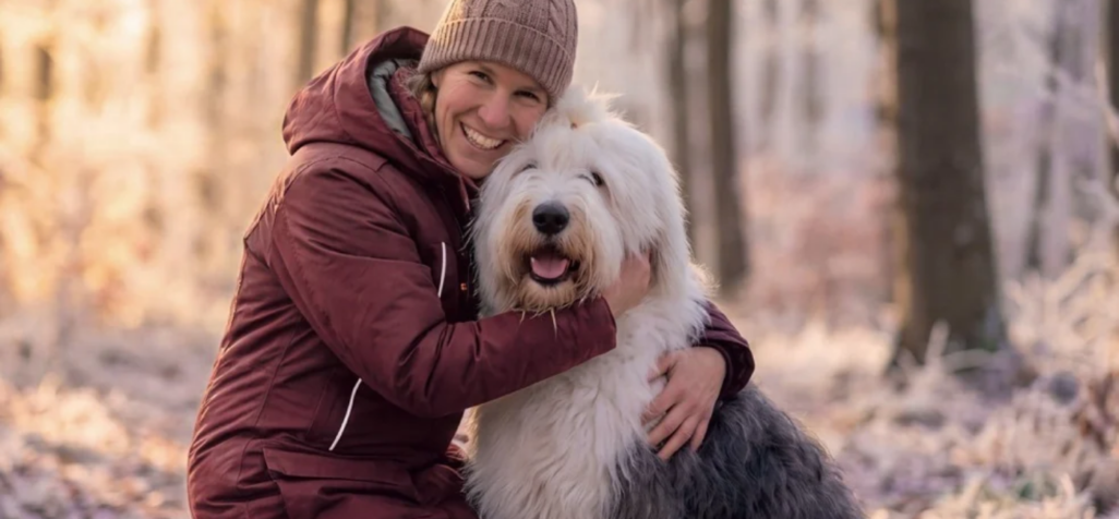 Frau kuschelt mit ihrem Bobtail Hund im Winter im Wald